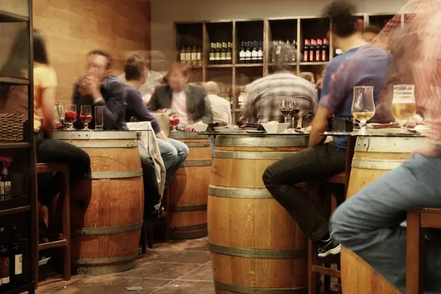 Clientes de pie alrededor de barricas usadas como mesas en una taberna.